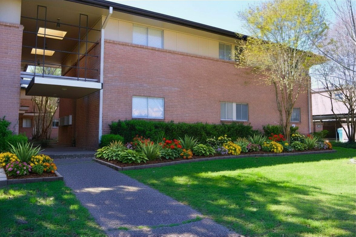 Two-story brick apartment building with landscaped garden beds along a walkway, Houston.