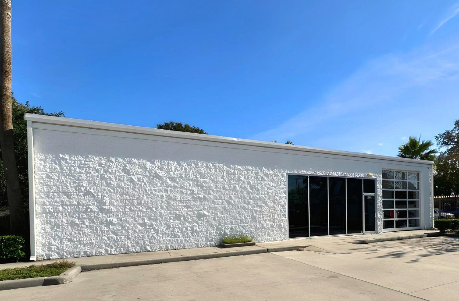 The exterior of the original auto-repair building, repainted white with the new glass storefront and roll-up door.